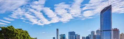 Clear blue skies in busy Australian city with green open space with deck chairs near canal and river. Background shows financial district with large modern office buildings.